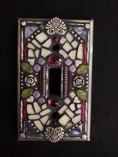 a decorative light switch plate cover with flowers and leaves on the front, sitting on a black surface