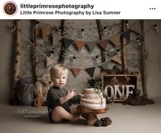 a little boy sitting on the ground with a cake in front of him and decorations around him