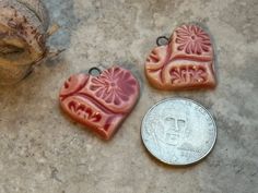 two heart shaped pendants sitting next to a penny