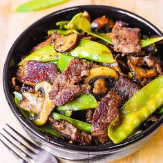 a bowl filled with meat and vegetables on top of a table next to a fork