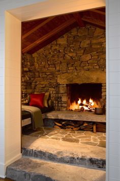 a stone fireplace in the middle of a room with a bed and pillows on it