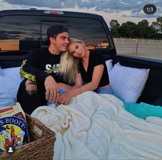 a man and woman sitting in the back of a pick up truck with blankets on it