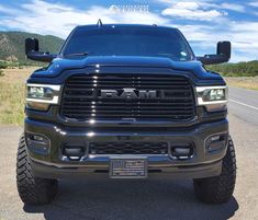 the front end of a black ram truck parked on a road with mountains in the background