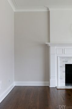 an empty room with a fireplace and hard wood flooring in the corner, painted white