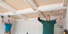 two men in green shirts are working on the ceiling