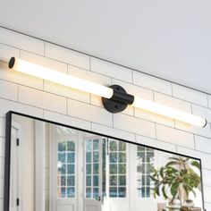 a bathroom mirror sitting on top of a white tiled wall next to a sink and window