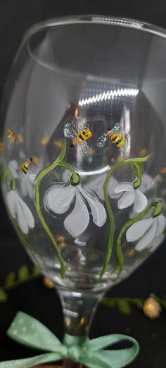 a wine glass with flowers painted on the bottom and green stems in the middle, sitting on a table