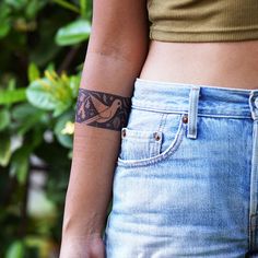 a woman with a tattoo on her left arm and tattoos on her right arm, standing in front of some bushes