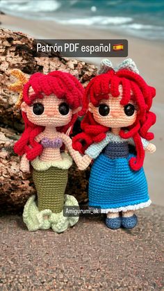 two crocheted little mermaids standing next to each other on the beach with water in the background