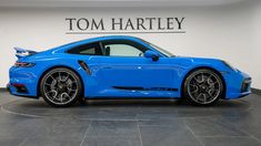 a blue sports car is parked in a showroom with the name tom hartley on it