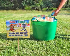 a green bucket filled with eggs next to a sign that says zuma and rocky's ready set get wet water balloon toss