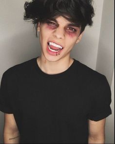 a young man with blood on his face and black t - shirt is standing in front of a white wall