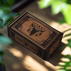 a wooden box sitting on top of a table next to green plants and leaves in the sunlight