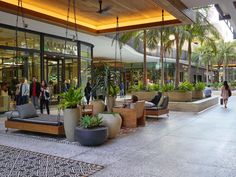 people are walking through the lobby of an office building with plants in large planters