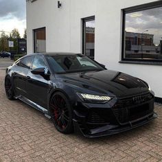 a black sports car parked in front of a white building with red rims on it