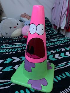 a pink and green cone sitting on top of a bed with stuffed animals in the background