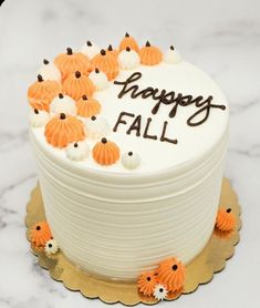 a white cake with orange frosting and happy fall written on the top is surrounded by small pumpkins