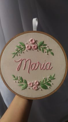 a hand holding up a small embroidered sign with flowers and the word monica on it