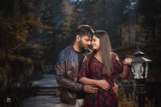 a man and woman standing next to each other near a lamp post with trees in the background