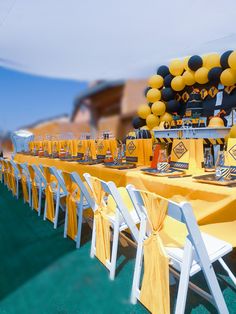 a table set up with yellow and black balloons, white chairs, and other decorations