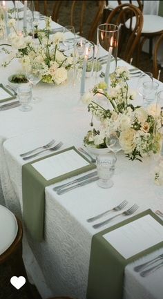 the table is set with white flowers and silverware