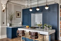 a large kitchen with blue cabinets and marble counter tops, along with two bar stools