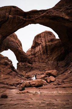 a man standing in the middle of a desert area under an arch shaped rock formation