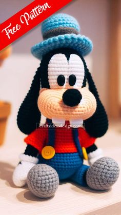 a crocheted mickey mouse with a blue hat and red shirt sitting on top of a table