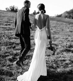 a bride and groom walking through the grass together in black and white photo with back to camera