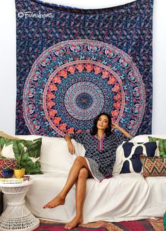 a woman sitting on a couch in front of a large tapestry hanging above her head