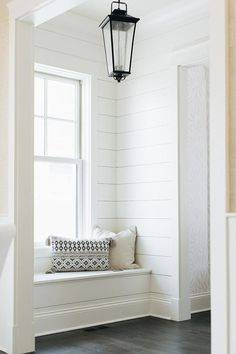 a lantern hanging over a window seat in a white room with black and white pillows