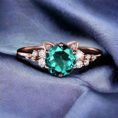 an emerald colored stone surrounded by white diamonds on a blue satin background with a rose gold ring