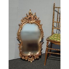 an ornate gold framed mirror sitting next to a chair and table with a green cushion on it