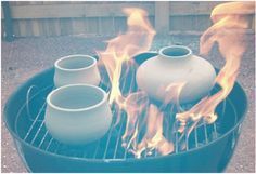 three white vases sitting on top of a bbq with flames coming out of them