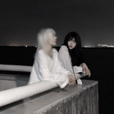 two women are sitting on a ledge at night