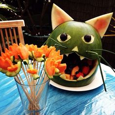 a watermelon cat with its mouth open next to some cut up fruit on a plate