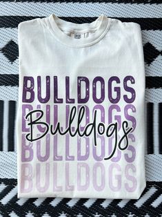 Get this popular new Bulldogs stacked text shirt and show off your school spirit in style!  Each shirt is printed in-house by me using high-quality materials on a Comfort Colors shirt, known for its exceptional comfort, style, and durability. Available in unisex sizes S to 3X, and youth sizes, we've got you covered regardless of your preferred fit. The Bulldogs stacked text Shirt features a classic crew neck and short sleeves, making it suitable for year-round wear. The flattering silhouette ensures a comfortable and stylish fit for both men and women. Please note that ivory is ONLY available in Adult sizes!  Note: As each shirt is individually printed, slight variations in color and placement may occur, adding to the uniqueness and charm of your Preppy Bulldogs Shirt. Your shirt will come School Spirit Shirt With Screen Print For Game Day, Casual Sublimation Design T-shirt With Letter Print For School, College Fan Apparel In Cotton With Sublimation Design, School Spirit Game Day Shirt With Screen Print, Screen Print Tops For College, White Collegiate Tops For School, School Spirit Shirt With Letter Print For Game Day, School Spirit Shirt With Letter Print, Back To School Spirit Shirt With Text Print