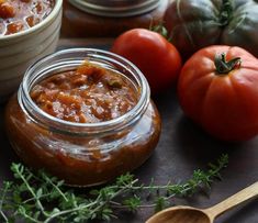 two jars filled with food sitting on top of a table next to tomatoes and other vegetables