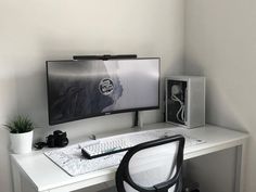 a white desk with a computer monitor, keyboard and mouse on it next to a plant