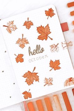 an open notebook with autumn leaves on it and the words hello october written in gold