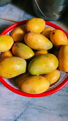 a red bowl filled with mangoes on top of a counter