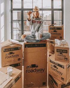 a woman sitting on top of boxes with her feet up in the air and drinking from a cup