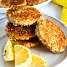 three crab cakes stacked on top of each other with lemon wedges next to them