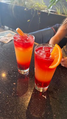 two cocktails sitting on top of a table with orange slices in the glass next to them