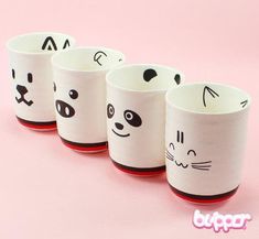 four white cups with black and red faces painted on the sides, lined up against a pink background