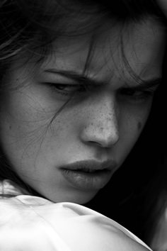 a black and white photo of a woman with freckles on her face looking down