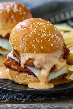 two burgers with cheese and onions on a black plate next to french fries in the background