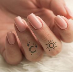 a woman's hand with two small tattoos on her fingers and one has a sun and moon