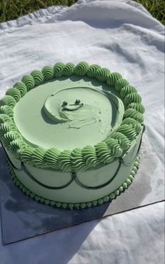 a green cake sitting on top of a white sheet covered table next to some grass