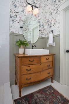 a bathroom with floral wallpaper and a wooden dresser in front of a mirror on the wall